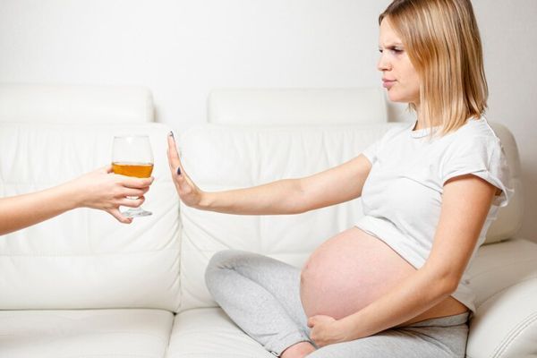 Mujer negando una copa de alcohol durante su embarazo, ya que podría causar problemas en el desarrollo del bebé