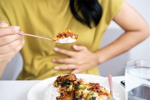 Helicobacter pylori - mujer en la mesa comiendo un plato de arroz con verduras agarrándose el estomago por un fuerte dolor