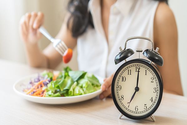 mujer comiendo una comida saludable con un despertador al lado