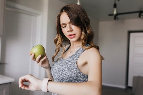 Una mujer con una manzana en la mano mirando el reloj esperando que sea hora de poder comersela