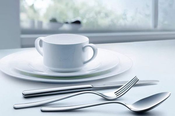 imagen de unos cubiertos sobre una mesa con platos y una taza