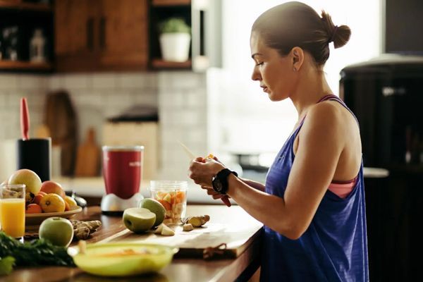 mujer vestida con ropa deportiva en la cocina de su casa preparando un batido de fruta y ginseng