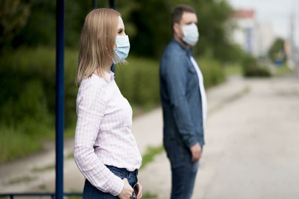 un hombre y una mujer en la parada del autobús con mascarilla para tapar la boca y manteniendo la distancia social de seguridad