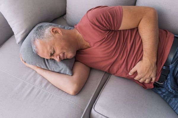 Helicobacter pylori - hombre con una camiseta de manga corta y unos jeans tumbado en el sofá con fuertes dolores en el estomago