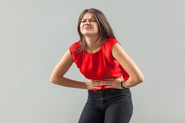 Helicobacter pylori - mujer vestida con unos jeans oscuros y una blusa sin mangas rojas agarrándose la tripa con las dos manos por unos fuertes dolores