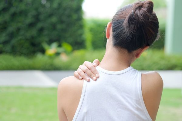 mujer en el jardín de espaldas agarrándose la clavícula con la mano como signo de cansancio o dolor