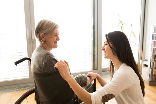mujer de rodillas hablando con una mujer mayor en silla de ruedas y ambas están sonriendo