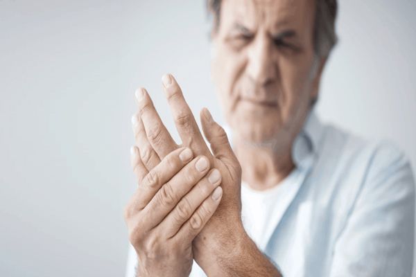 Esclerosis múltiple - hombre mayor agarrándose la mano con signos de fuertes dolores en su rostro