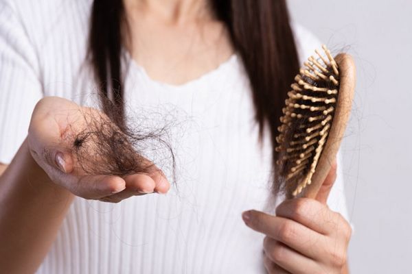Vitamina D - mujer con un mechón grande de pelo en la mano derecha y en la izquierda el cepillo con más restos de pelo tras el cepillado
