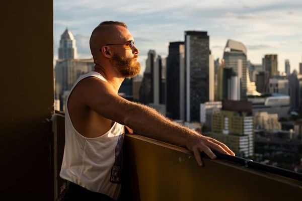 hombre con camiseta de tirantes blancas y gafas de sol, en el balcón de su casa tomando el sol