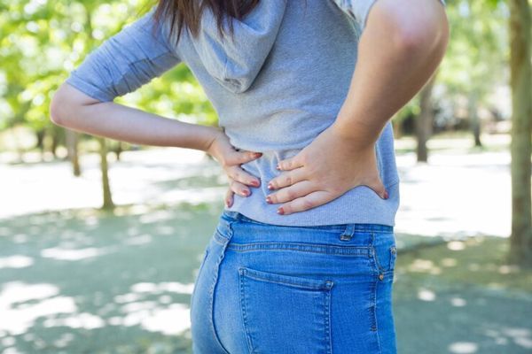 mujer blanca en el parque agarrándose la zona de los riñones por los dolores