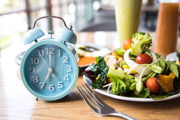 Ayuno intermitente - Platos de comida saludable al lado de un despertador con unos vasos de jugo