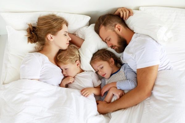 Melatonina - una familia formada por el padre, la madre, y un niño y una niña duermen plácidamente en la misma cama