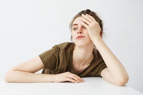 Lupus - mujer joven blanca sentada delante de una mesa y sujetando su cabeza con la mano y el brazo apoyado en la mesa