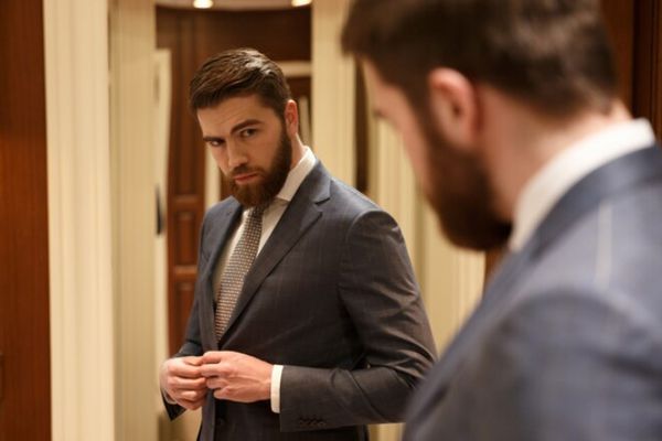 Trastorno de la personalidad narcisista - hombre joven bien vestido con traje, el pelo y la barba arreglados y mirándose en el espejo