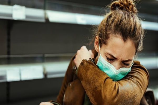 COVID19 - mujer blanca con mascarilla y chaqueta de piel tapándose la boca con el brazo mientras tose