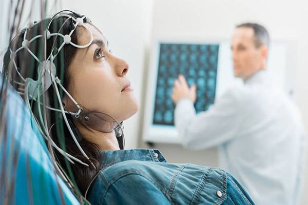 Esclerosis múltiple - mujer tumbada en la camilla sometiéndose a una prueba de potenciales evocados bajo la atenta supervisión del especialista