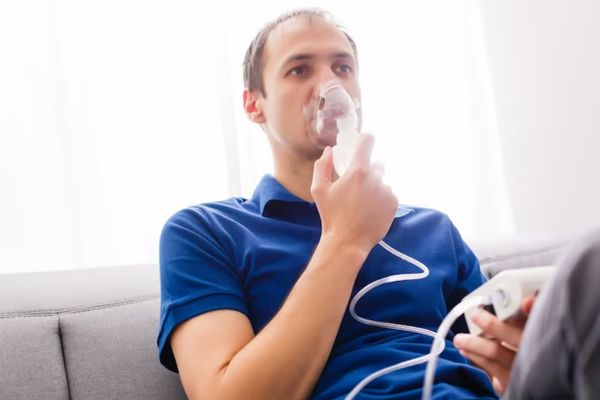 hombre joven en el sofá de su casa con un dispositivo para suministrarle oxigeno para respirar
