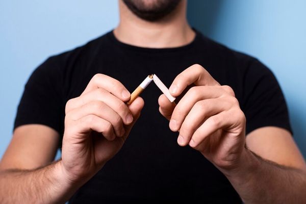 imagen de un hombre blanco con una camiseta de manga corta negra rompiendo un cigarrillo
