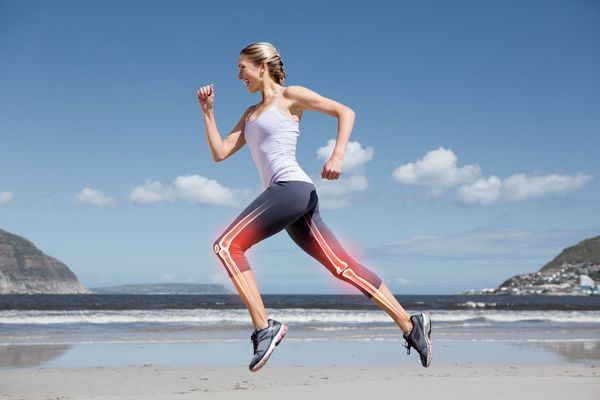Vitamina D - mujer con ropa deportiva corriendo por la playa con la imagen de los huesos de las piernas superpuestos en la zona de las piernas