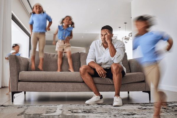 TDAH - Padre estresado por la hiperactividad de sus hijos, los cuales brincan y juegan por toda la casa