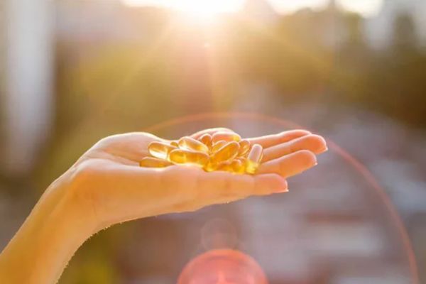 Vitamina D - mujer mostrando en las manos unas píldoras con el sol saliendo entre los edificios