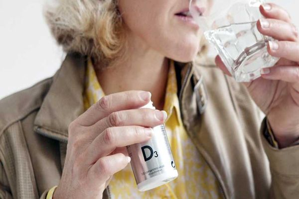 mujer bebiendo un vaso de agua con un bote de un suplemento vitamínico de vitamina D en la mano derecha