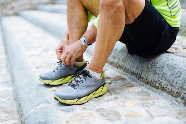 hombre vestido con ropa para correr sentado en unas escaleras de piedra mientras se ata las deportivas