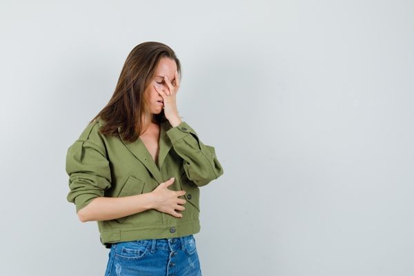 Diverticulitis - mujer blanca de pie con una mano en la cara y otra en el abdomen con fuertes dolores en el vientre