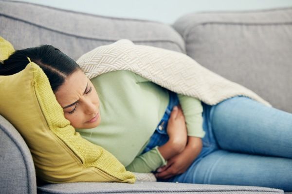 Endometriosis - Mujer acostada en el sofá para intentar aliviar el dolor pélvico, el cual presenta debido a la afección en los tejidos del útero