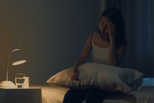 Melatonina - joven sentada en la cama con la almohada en regazo preocupada por sus problemas para dormir