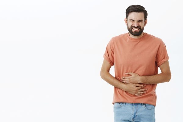 hombre agarrándose el vientre con las dos manos por fuertes dolores en el abdomen