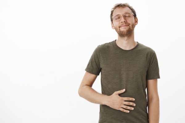 Diverticulitis - hombre blanco delgado con la mano sobre su abdomen con cara de satisfacción