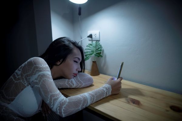 mujer con problemas para dormir apoyada en mesa mirando el teléfono móvil