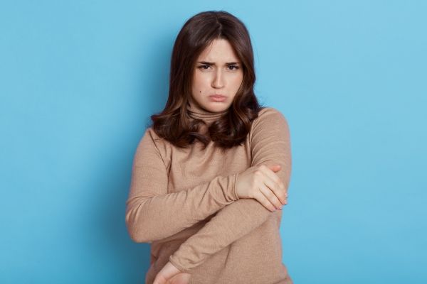 mujer con cara triste y un polo de manga larga agarrándose el brazo a la altura del codo