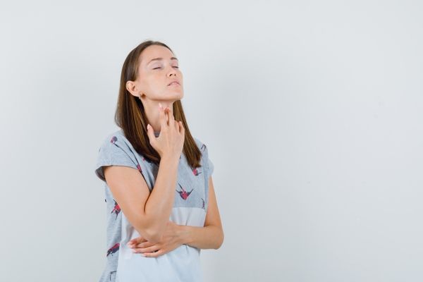 mujer joven en pijama y un delantal tocándose la garganta por las molestias que sufre por culpa de la enfermedad