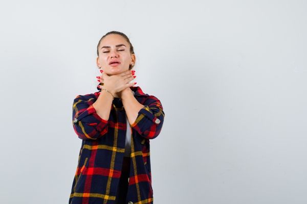 Disfagia - mujer joven con una camisa a cuadros agarrándose la garganta al sentir como el bolo alimentario no pasa