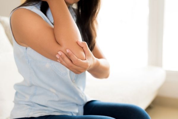 Mujer con un fuerte dolor en el codo debido a la inflamación de las bolsas sinoviales, causado por apoyar el brazo en una superficie dura por un tiempo prolongado