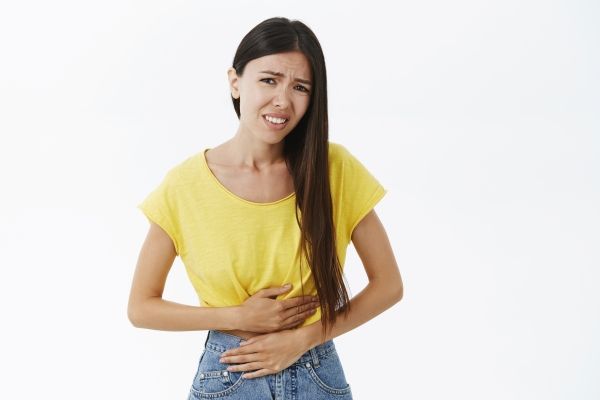 mujer blanca de pie con las dos manos en el abdomen con fuertes dolores en el vientre