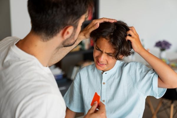 Pediculosis - Padre ayudando a su hijo a quitar los piojos que tiene en el cabello, debido a una infestación que adquirió en el colegio