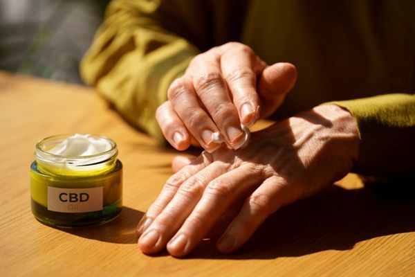 CBD - mujer mayor usando una crema con aceite de CBD para los dolores de la mano