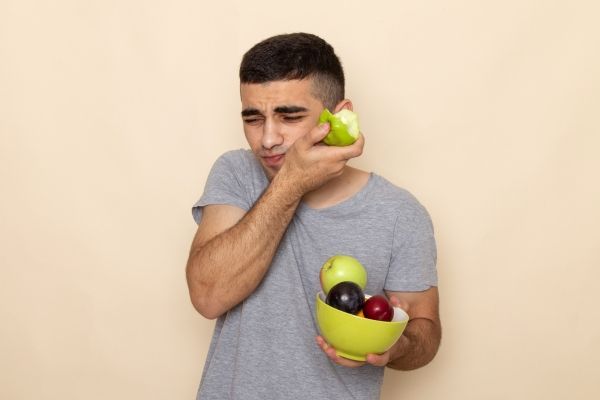 Disfagia - hombre joven comiéndose una manzana mostrando problemas para poder tragar la comida