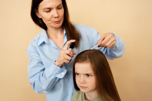 Pediculosis - Madre aplicando un tratamiento en el cabello de su hija, para eliminar los piojos y liendres del cuero cabelludo