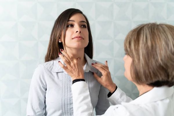 Hipertiroidismo - Especialista en su consulta palpando la tiroides de una paciente para diagnosticar si existe algún problema