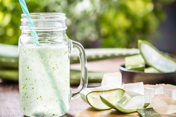 mesa con hojas de aloe vera enteras y cortadas en porciones al lado de un batido de aloe vera y miel