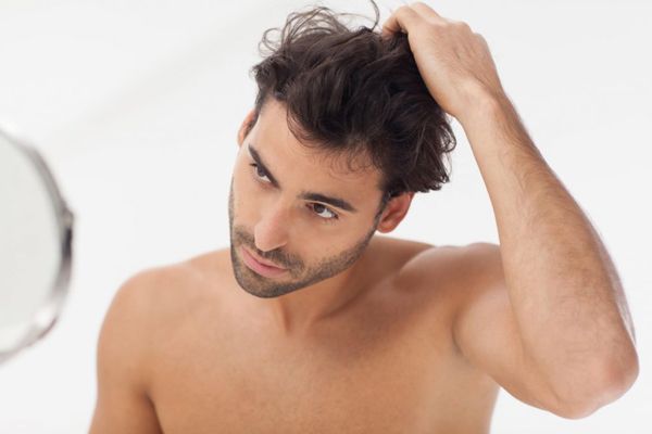 Hombre en el baño revisando y acariciando su cabello delante del espejo