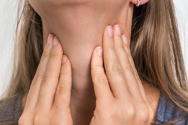 Hipotiroidismo - mujer rubia con sus manos en el cuello masajeando la zona donde se encuentra la tiroides 