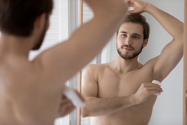 Hiperhidrosis - Hombre en el baño poniéndose desodorante en barra en los sobacos