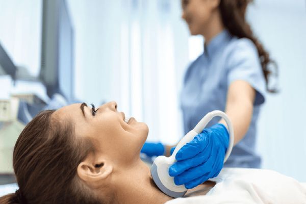 Mujer sonriente en la consulta de la especialista sometiéndose a una ecografía tiroidea 