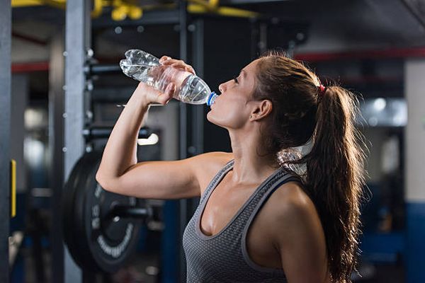 Mujer en el gimnasio tomando agua para mantenerse hidratada durante el ejercicio